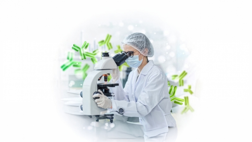 Lab technician in a white coat, safety cap, and mask working with a microscope in a science lab, with stylized graphic representations of molecules or antibodies in the background