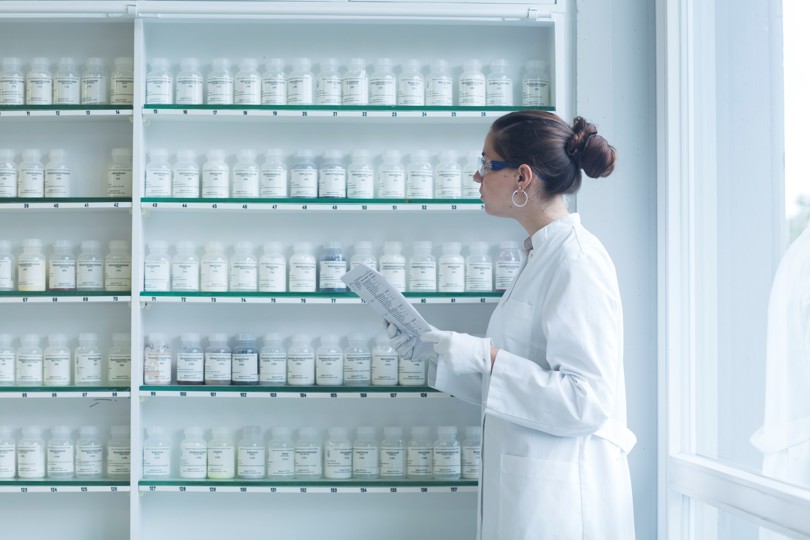 Woman in white lab coat inspecting various bottles in a lab