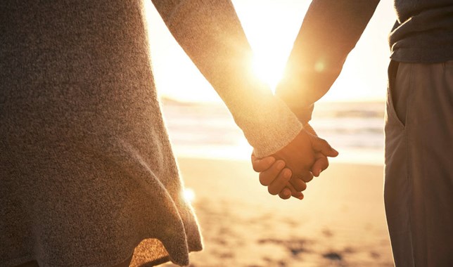 Couple holding hands on beach at sunset striving for emotional and physical intimacy after cancer treatment.