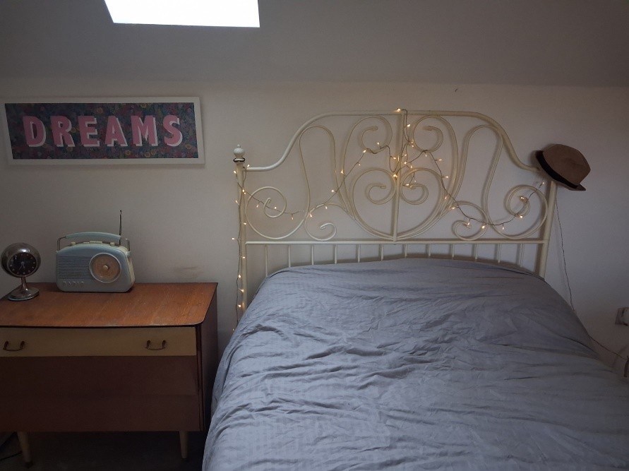 Spare bedroom with a single bed, fairy lights on the headboard, and a radio for classical music.