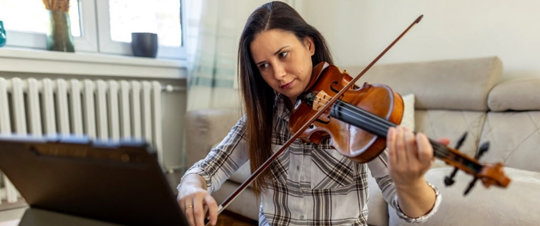 Woman sitting in living room with her violin taking an online lesson and enjoying positive effects on mental health and wellbeing