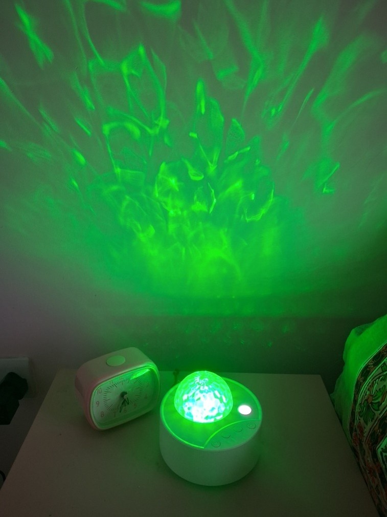 Northern lights-type green pattern projected onto a wall by bedside color-pattern lamp.