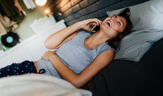 Woman chatting on phone in bed to a member of her migraine support group