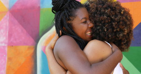 Women hugging in front of a colorful wall Women hugging in front of a colorful wall