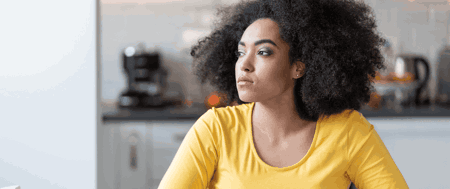 A woman with an afro sits at a table, reflecting on her journey to overcome depression and isolation.